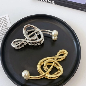 Close-up of gold and silver musical note hair claws with white pearls on a tray