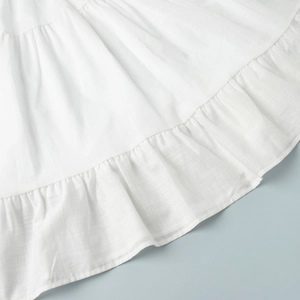 Detailed view of the white cotton dress featuring layered ruffle hem and woven texture