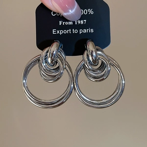 Close-up of layered silver-tone hoop earrings made of copper on a black display card