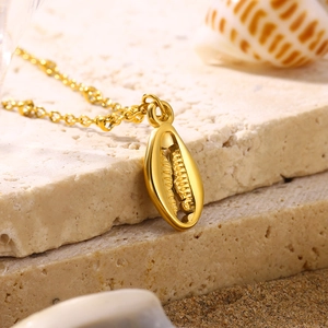 Close-up of a golden shell pendant on a fine chain over beach stones and sand background