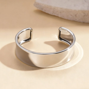 Close-up of wide open cuff bracelet in polished silver metal on minimalist stone background