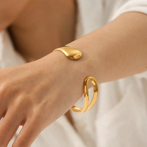 Close-up of a minimalist golden teardrop bangle with a smooth streamlined open design