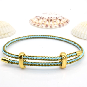 Detail of adjustable blue and gold braided rope bracelet with metallic clasp and shells