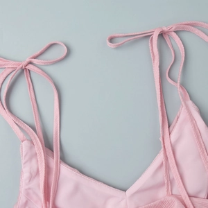 Detail of pink ruffled top with adjustable shoulder straps tied in delicate bows