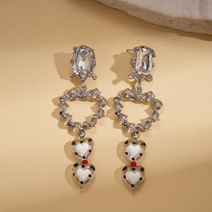 Boucles d'oreilles cœur argentées avec strass et pois noirs sur un fond en pierre