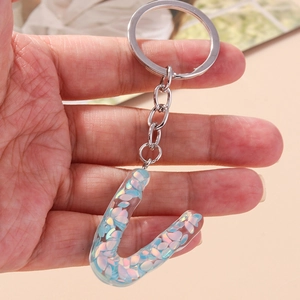 Detail of transparent resin letter J keychain with blue iridescent sequins and silver ring