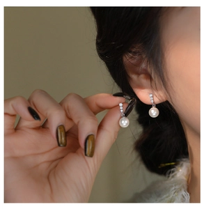Detailed close-up of a model wearing a pair of French style white pearl earrings with zircon