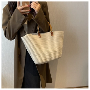 Detailed close-up of natural bamboo handle on woven beige tote bag with leather straps