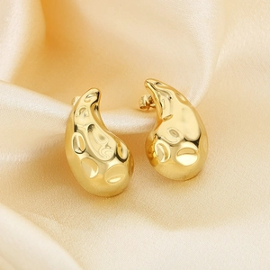 Macro shot of gold teardrop earrings with hammered texture on champagne silk