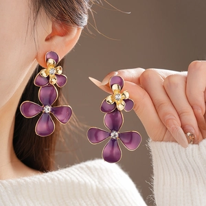 Macro detail of purple enamel flower earrings with gold edges and crystal center