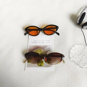 Flat lay of cat-eye sunglasses in black with orange lenses and tortoise shell frames