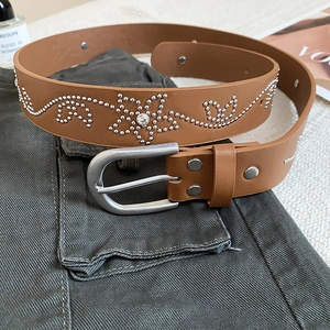 Détails de la ceinture en cuir marron avec rivets argentés, motifs floraux et strass