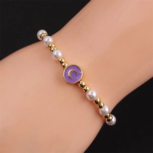 Detail showing the beaded bracelet with white pearls and gold moon pendant on a wrist