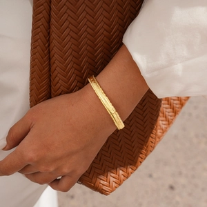Detail showing 18k gold plated bangle with horizontal textured finish on a model's wrist