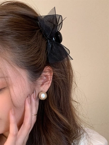 Detail shot of black mesh bow hair clip and elegant champagne pearl earrings on a model
