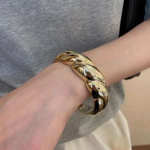 Close-up of a chunky gold twisted knot cuff bracelet showing metallic texture