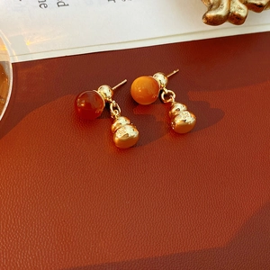 Macro detail of retro gold gourd earrings with amber beads on brown leather background
