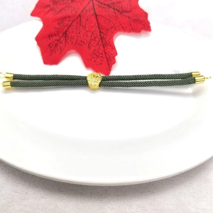 Detail of dark green Milan cord bracelet with 18k gold-plated beads on a white plate