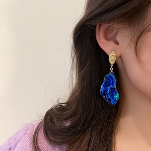 Close-up of a model wearing a gold textured earring with a dark blue irregular resin pendant