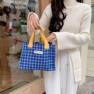 Blue plaid canvas lunch bag with bright yellow handles shown in a lifestyle street setting