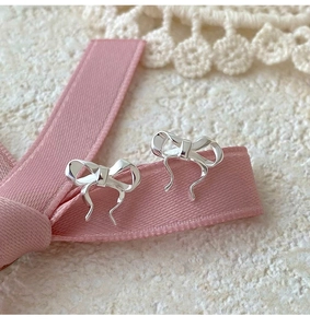 Macro shot of silver bow stud earrings on pink ribbon with white lace background