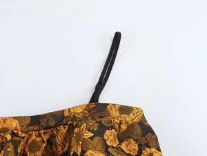 Dettaglio delle spalline nere sottili su un top corto in jacquard marrone dorato