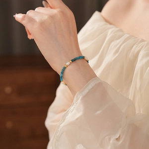 Detail of blue stones and freshwater pearls bracelet on a model's wrist with golden beads