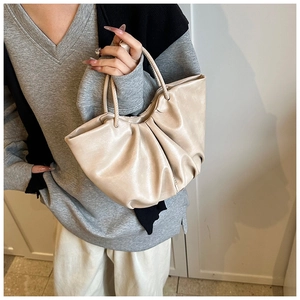 Detail of soft pleated beige cloud bag with elegant slim double top handles and leather texture