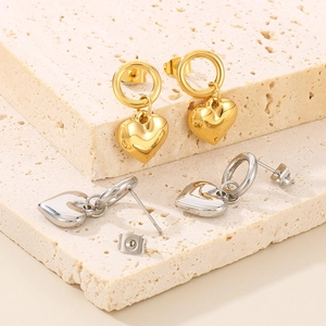 Polished heart pendant earrings in gold and silver set on a decorative beige stone
