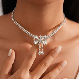 Close-up of a silver bow necklace with sparkling crystals and water drop tassels on a model