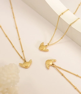 Detail view of gold bead chain necklaces featuring winged disc pendants on a white podium