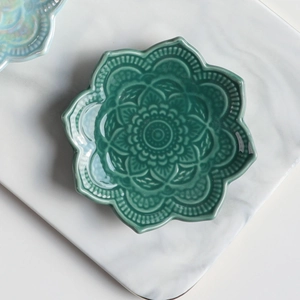 Detailed top view of a dark green mandala ceramic jewelry tray on marble background