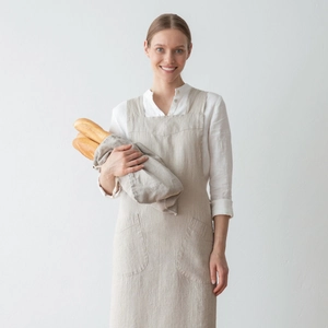 Detail of light beige linen apron featuring two large front pockets and cross-back straps