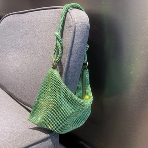 Close-up of emerald green rhinestone handbag with full crystal mesh on grey fabric chair