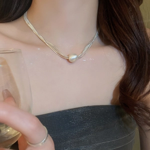 Detail of silver layered snake chain necklace featuring a large white pearl pendant on model