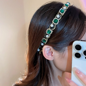 Close-up of model wearing emerald green gems and pearl headband in golden alloy setting