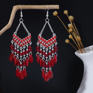 Dettaglio artistico di orecchini boho con nappe di perline rosse appesi a un ramo di legno