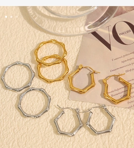 Close-up of gold and silver bamboo-style hoops and hexagonal earrings on textured fabric