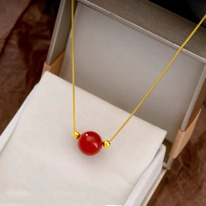 Detailed view of red agate pendant necklace with gold beads inside a gray jewelry box