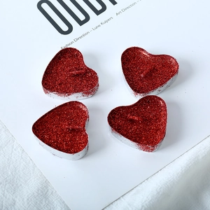 Set of four heart-shaped red glitter tea light candles with metal holders on white fabric