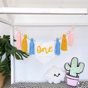 Detail of baby birthday banner with colorful tassels and a white linen 'one' flag