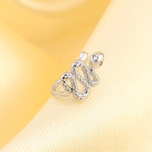 Macro shot of a silver snake-shaped ear cuff with small diamond on yellow silk background