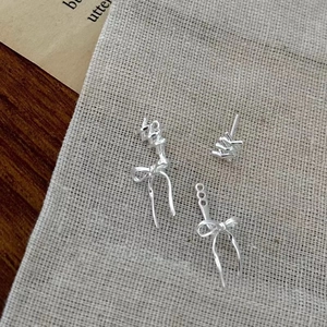 Detailed view of silver bowknot and irregular letter earrings on beige linen