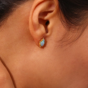 Detailed macro view of a gold-plated teardrop opal earring worn on the earlobe
