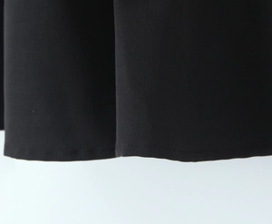 Dettaglio dell'orlo del vestito nero con cuciture precise e trama del tessuto