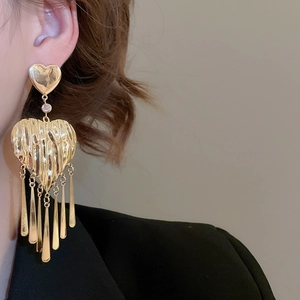 Detail of large gold heart tassel earring with lava texture worn by a model