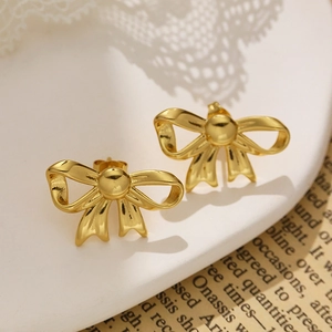 Close-up of golden bow-shaped stud earrings with polished metallic texture on a white tray