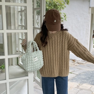 Detail of light green pleated bubble fabric handbag paired with a brown knit sweater