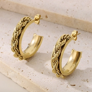 Close-up of golden twist rope C-shaped hoop earrings on natural stone background