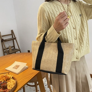 Handwoven straw tote bag with black fabric handles in a natural interior setting